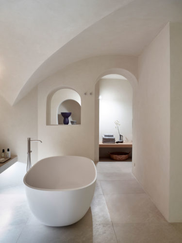 An open plan bathroom with bathtub and a separate bathroom with steam/hammam bath.